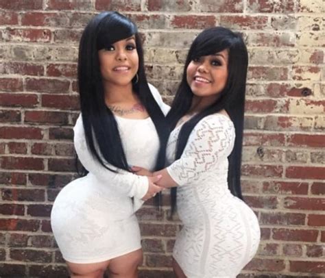two women standing next to each other in front of a brick wall with long black hair