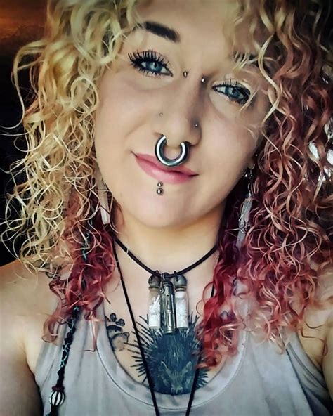 A Woman With Long Curly Hair And Piercings On Her Nose Is Smiling At The Camera