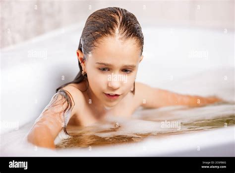 Little Cute Caucasian Girl Bathes In A Bathtub With Foam And Has Fun During Quarantine At Home
