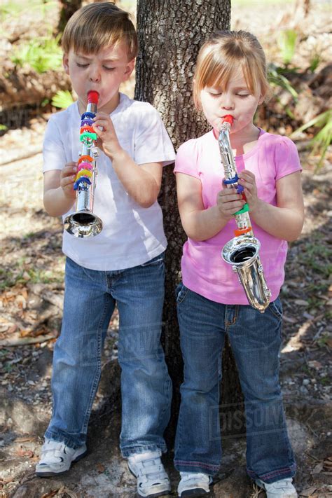 A Boy And A Girl Standing By A Tree And Playing Toy Musical Instruments