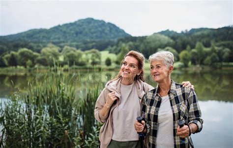 happy senior mother embracing with adult daughter when standing by lake outdoors in nature stock