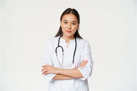 Портрет азиатской женщины врача скрестив руки стоя в медицинской форме и стетоскопе улыбаясь