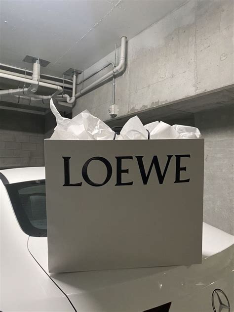 A White Car In A Parking Garage With A Sign That Says Loewe On It