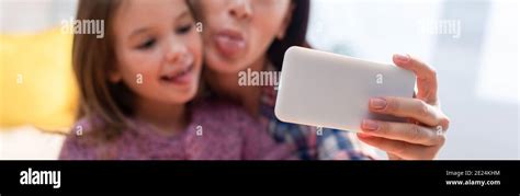 Mother And Daughter With Sticking Out Tongues Taking Selfie On Blurred
