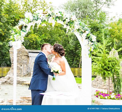 First Kiss Of Newly Married Couple Under Wedding Arch Stock Photo