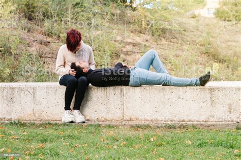 Young Man Lying Relaxed On A Wall In The Park With His Head On His