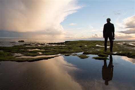 Silhouette Of Man Standing On Rock Formation Near Body Of Water During