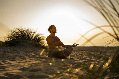Shirtless Man Meditating While Practicing Yoga On Sand At Beach Against