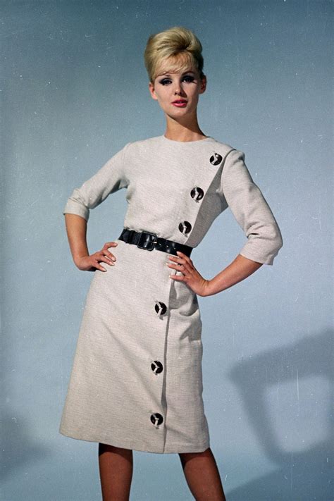 1962 A Model In A Taupe High Neck Dress With Three Quarter Length Sleeves And A Waist Cinching