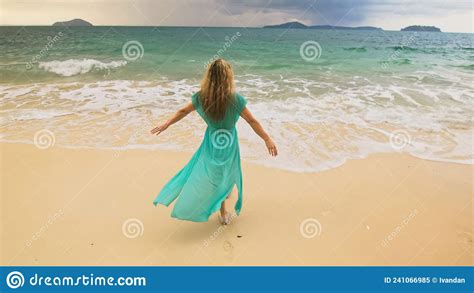 woman walks to the stormy cloudy ocean on sand beach girl in blue swimsuit dress tunic stock