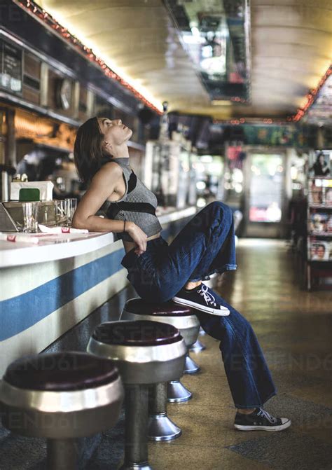 side view of woman wearing jeans and sleeveless top leaning against a bar counter in a