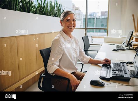 Friendly Receptionist Smiling At Camera While Sitting At Desk With