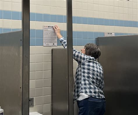 A Maintenance Worker Installs A Not Alone Sign In Restroom Stalls