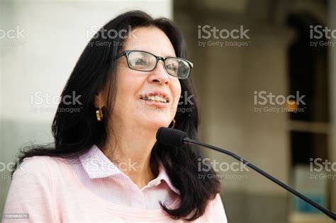 Mature Latina Woman Smiling At Crowd During Speech Over Microphone