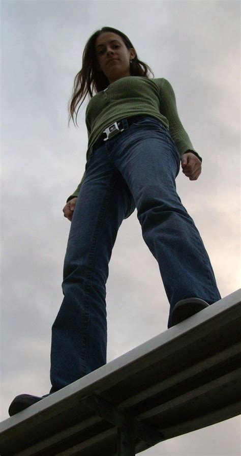 a woman standing on top of a metal roof with her hands in the air while wearing jeans