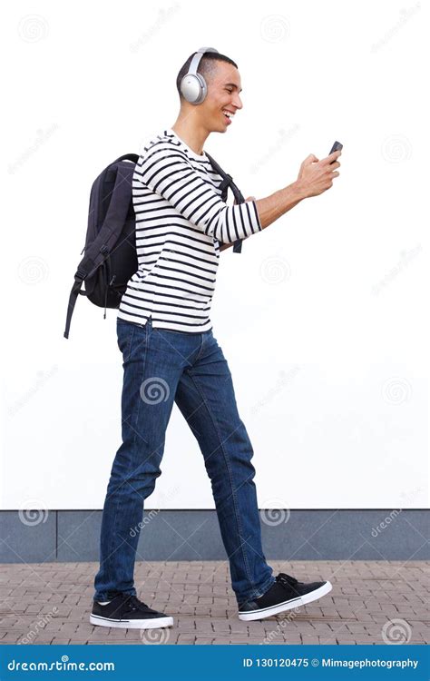 Profile Of Young Man Walking And Looking At Cellphone While Listening