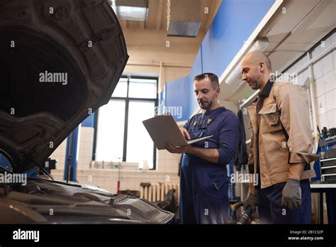 Side View Portrait Of Two Car Mechanics Using Laptop While Inspecting