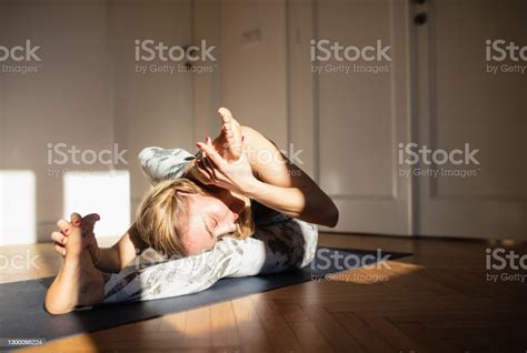 Woman Doing Yoga At Home With One Leg Behind Her Head Leaning Head On
