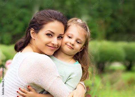 Beautiful Mother Hugging And Kissing Her Cute Small Daughter On Summer Green Grass Background