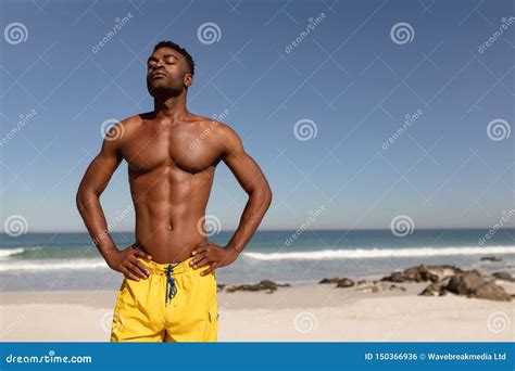 Shirtless Man With Hands On Hip And Eyes Closed Standing On Beach In