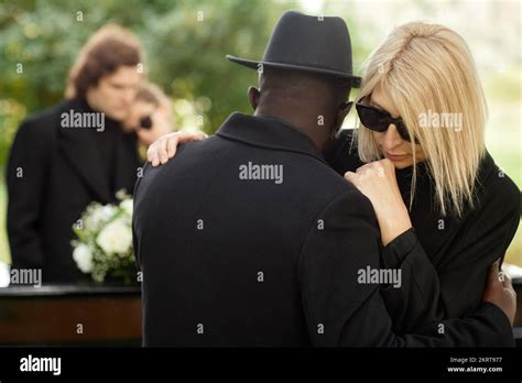 Two people embracing at outdoor funeral ceremony and wearing black