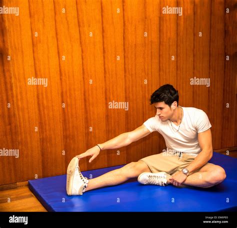 Attractive Young Man Stretching On Gym Mat Touching Foot With Hands