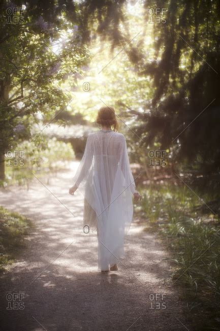 A Woman Dressed In A Sheer White Dress Walking Down A Wooded Garden