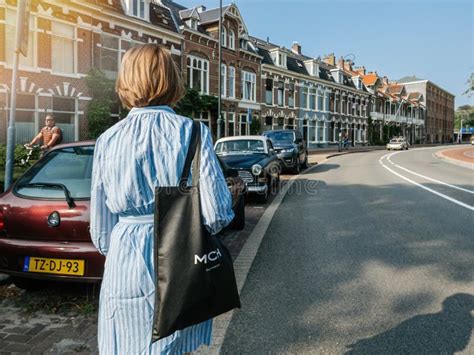 utch woman walking on the large dutch street with traditional townhouses in the editorial