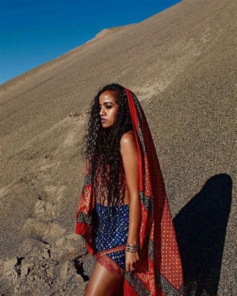 A Woman Standing On Top Of A Hill In A Blue And Red Dress With An Orange Shawl Over Her Head