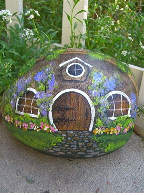 A Rock With A House Painted On It Sitting In Front Of Some Plants And