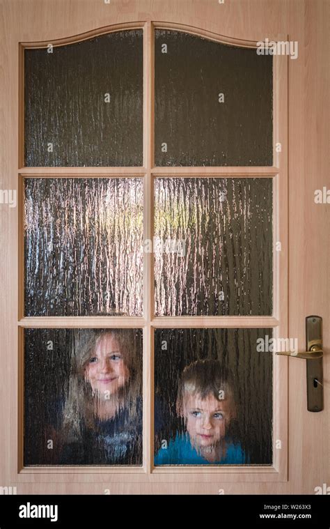 Portrait Of A Cute Little Caucasian Boy And Girl Hiding Behind A Door