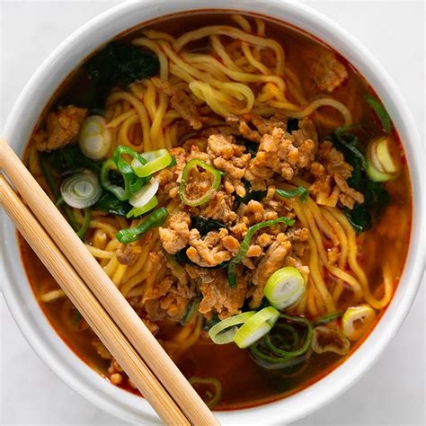 A White Bowl Filled With Noodles Meat And Veggies Next To Chopsticks