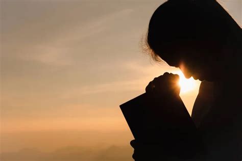 Silhouette Of Christian Young Woman Praying With Holy Bible At Sunrise