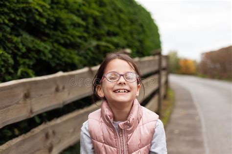 Little Beautiful Cute Girl In Glasses Laughing Near A Wooden Fence