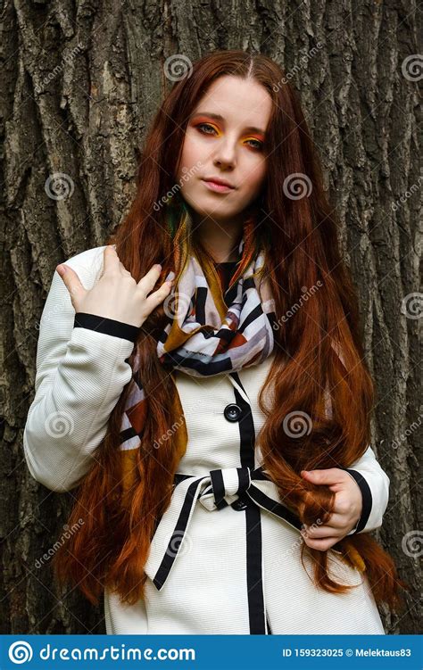 Woman With Long Red Hair And Bright Makeup Near A Tree Stock Image