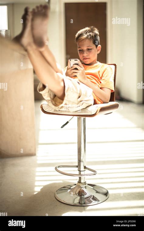 A Boy Sitting Looking At A Mobile Phone Screen With Feet Up On A