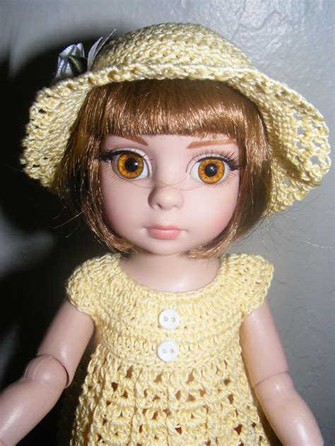 a close up of a doll wearing a yellow dress and hat with big brown eyes