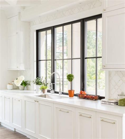Brushed gold faucets are fixed to a white quartz countertop accenting a brown brushed oak dual bath vanity finished with brass hardware. Beautiful kitchen features white cabinets adorned with ...
