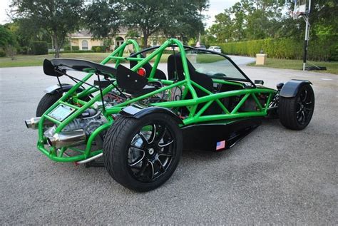 A Green And Black Race Car Parked In A Parking Lot Next To A Tree Lined