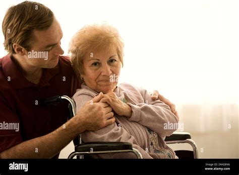 Portrait Of A Happy Elderly Woman Being Assisted By A Male Nurse Stock