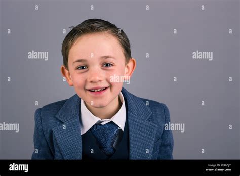 Portrait Of 8 Year Old Boy Dressed In Suit Smiling Isolated On Gray