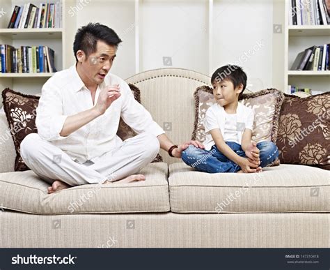 Father And Son Having A Conversation On Couch At Home Stock Photo