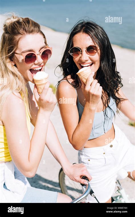 Happy Blonde And Brunette Girls Riding Bikes And Eating Ice Cream Stock