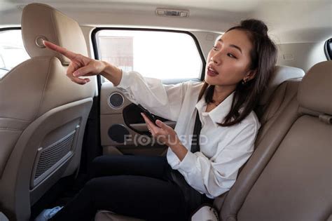 Side View Of Ethnic Female Passenger With Smartphone Riding On Backseat In Taxi And Showing