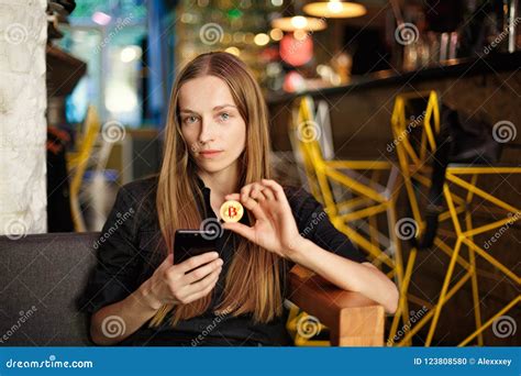 Young Woman With A Bitcoin And Smartphone Sits In A Cafe Stock Photo