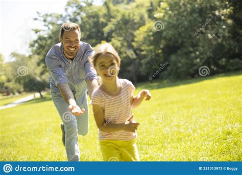 Father Chasing His Little Daughter While Playing In The Park Stock