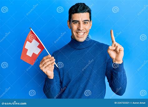 Handsome Hispanic Man Holding Switzerland Flag Smiling With An Idea Or