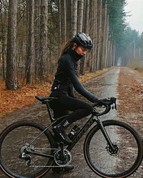 A Woman Riding A Bike On A Wet Road In The Woods With Trees Behind Her