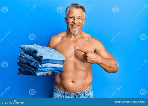 Middle Age Grey Haired Man Shirtless Holding Stack Of Folded Jeans Smiling Happy Pointing With
