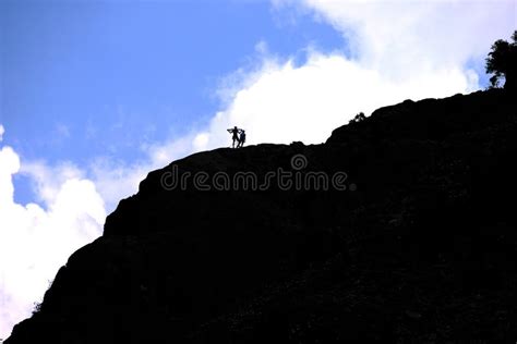 Silhouette Of Two Climbers On A Mountain Top With A Flag In His Hand